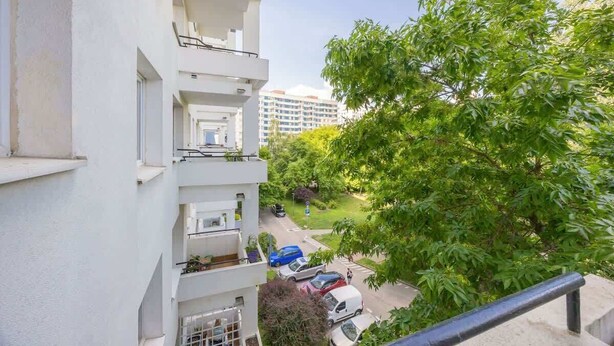 A multi-story residential building with balconies, a parking area, and a green park with trees. - Bright Apartment with Balcony | Workplace, Close to Metro (Warszawa)