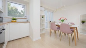 A modern kitchen with white cabinets, a wooden countertop, and a window. There is a dining area with a table, chairs, and a vase of flowers. - Bright Apartment with Balcony | Workplace, Close to Metro (Warszawa)