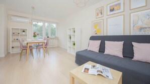 A modern living room with a grey sofa, a dining table with chairs, and a bookshelf. - Bright Apartment with Balcony | Workplace, Close to Metro (Warszawa)
