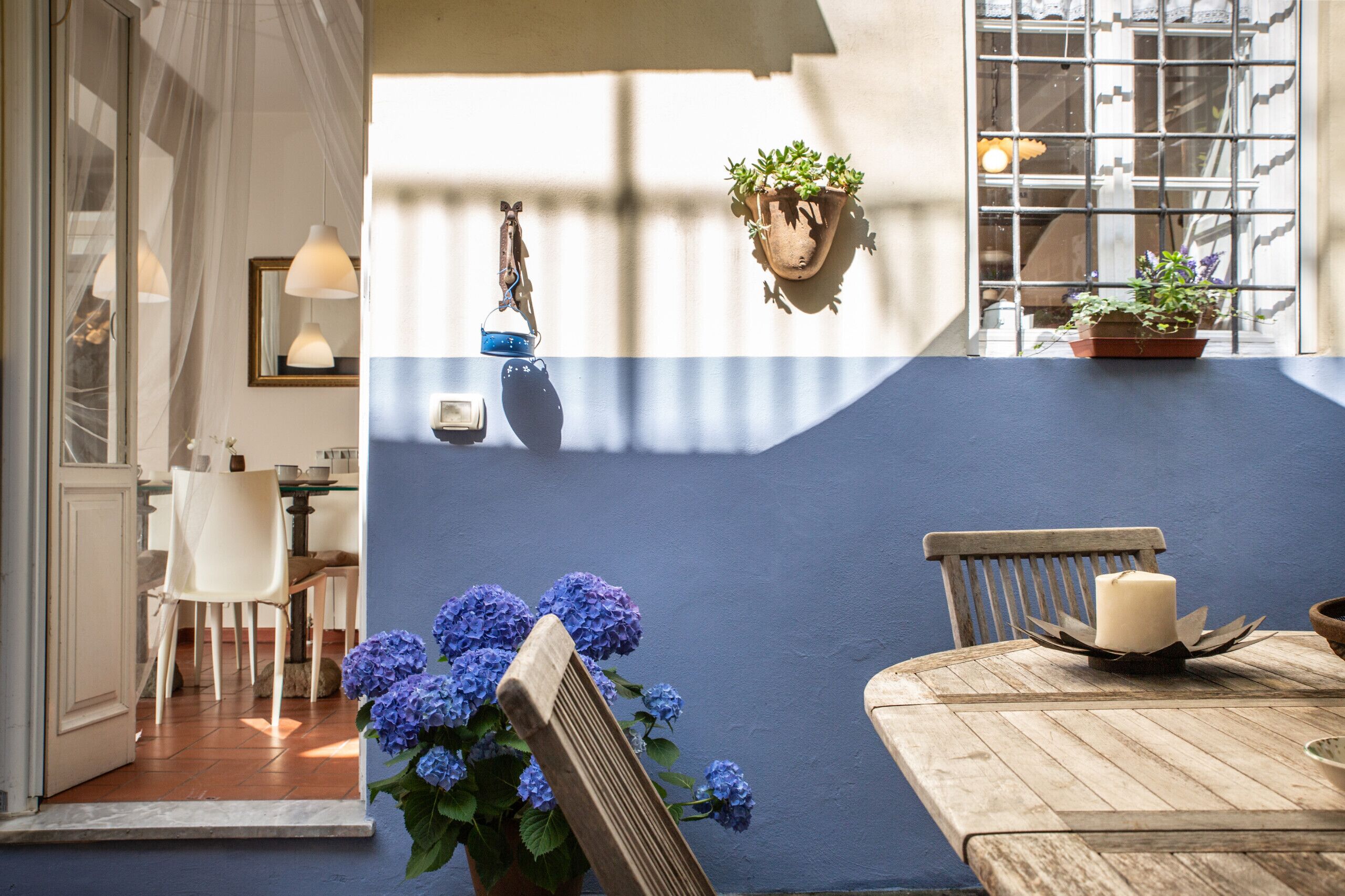A dining area with a wooden table, chairs, and a candle centerpiece. There are potted plants and a hanging light fixture.