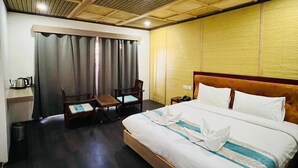 A hotel room with a wooden ceiling, a bed with white bedding, a wooden nightstand, a chair, a desk with a kettle, and a trash bin. - Thongsal (Leh)