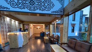 A wooden interior with a reception desk, seating area, and large windows. - Thongsal (Leh)