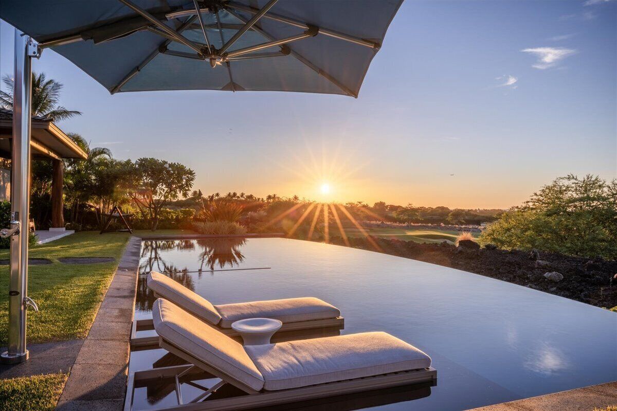 Ein Infinity-Pool mit Liegestühlen und Sonnenschirm mit Blick auf einen Sonnenuntergang.