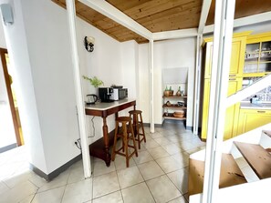 Una cucina con un tavolo di legno, sgabelli, un forno a microonde e uno scaffale con utensili da cucina.