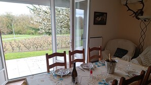 A dining area with a table set for two, a bottle of champagne, and a view of a vineyard through large windows. - Pleine Nature, Maison de Campagne à 10 min zoo Beauval Mareuil/cher (Mareuil-sur-Cher)