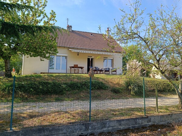 A two-story house with a tiled roof, a front porch with a table and chairs, and a fenced yard.