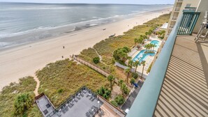Vue sur la plage depuis le balcon d’un hôtel, avec une piscine et un espace salon extérieur.