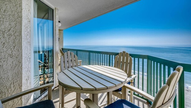 Un balcon avec une table et des chaises, donnant sur une plage.