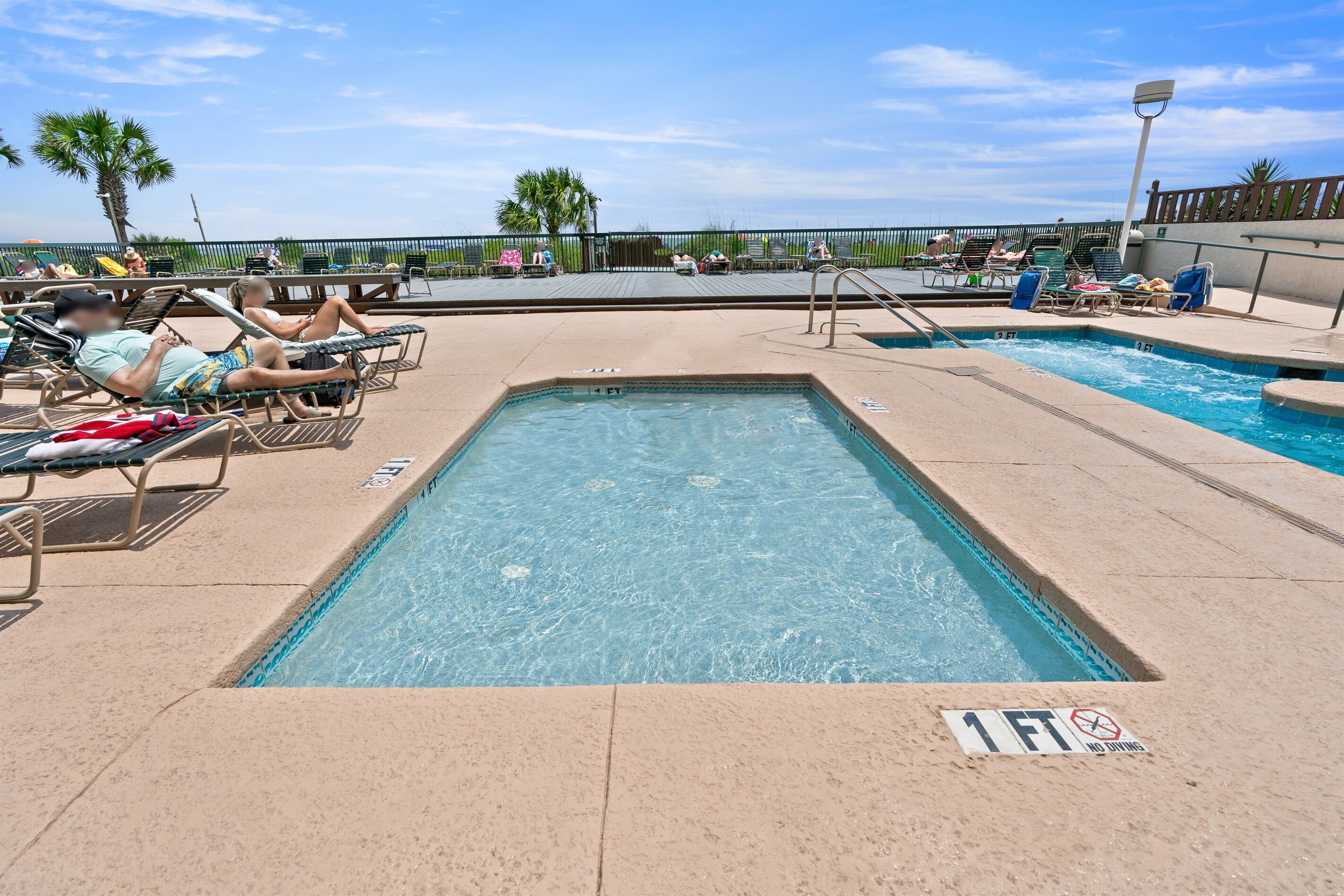 A pool area with lounge chairs and a sign indicating a 1-foot depth.
