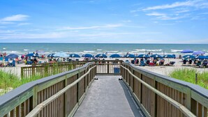 Une promenade en bois menant à une plage où l’on trouve des parasols et des chaises de plage.