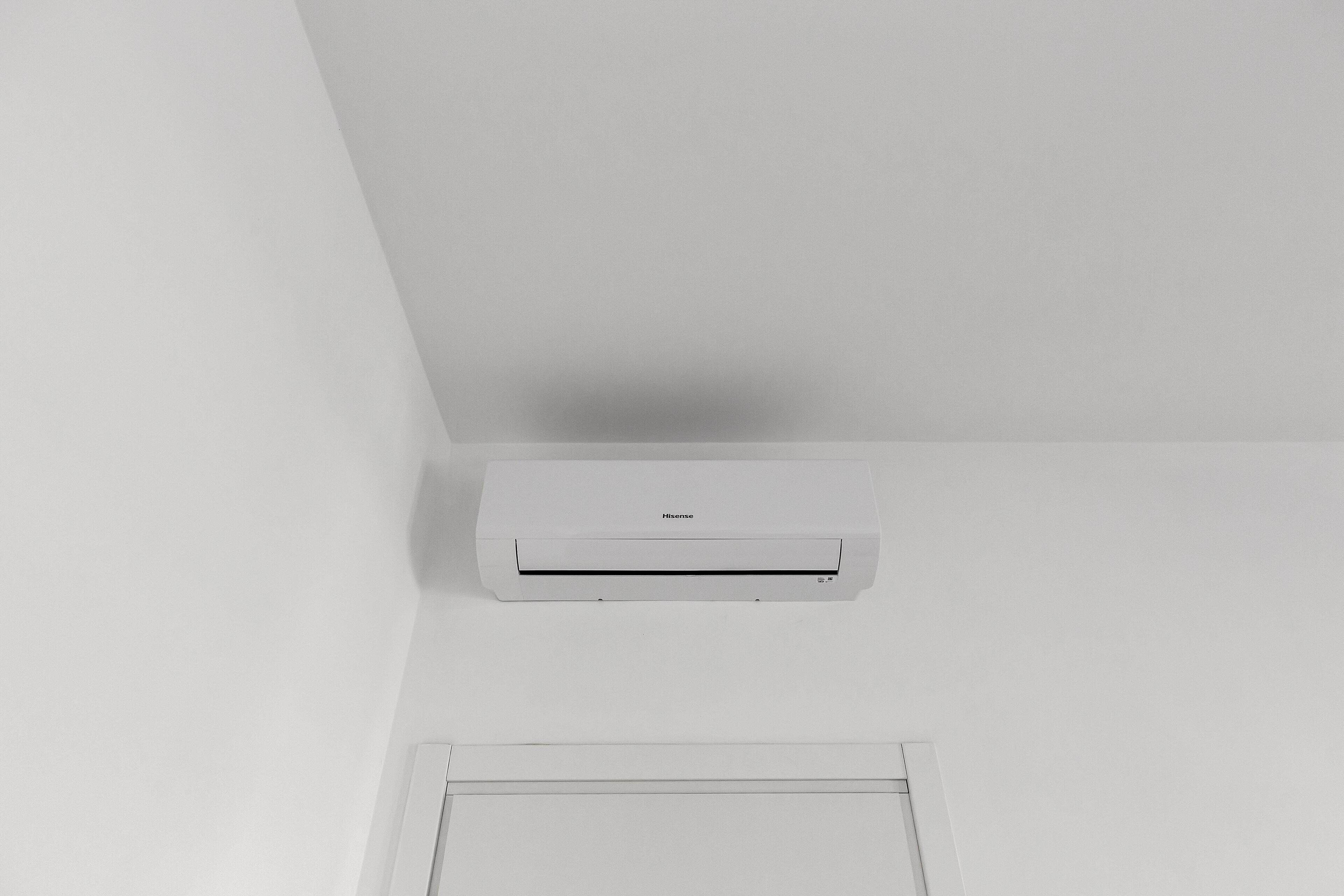 Un appareil de climatisation blanc est fixé au plafond blanc d’une pièce aux murs blancs.