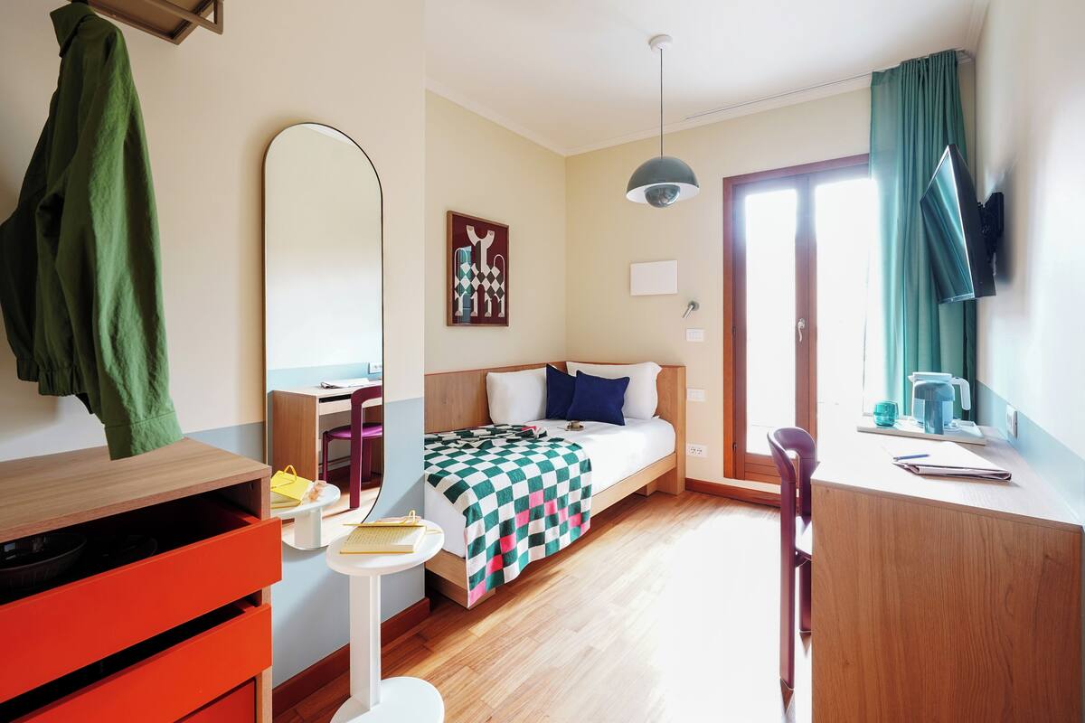 A modern hotel room with a bed, desk, chair, and a large mirror.