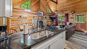 Ein rustikales Blockhaus im Inneren mit Kamin aus Naturstein, Holzwänden, einer Küche mit Granit Arbeitsplatten und einem großen Fenster.