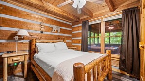 Ein Schlafzimmer in einer Holzhütte mit einem Bett, einem Nachttisch, einer Lampe und einem Fenster mit Vorhängen.