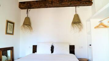 A bedroom with a wooden headboard, a bed with white bedding, and two hanging light fixtures.
