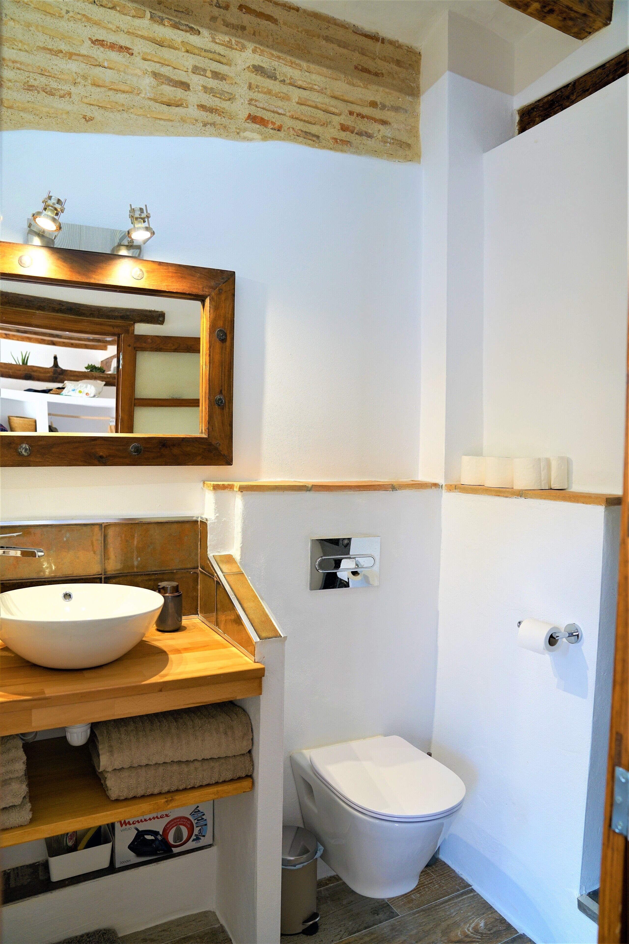 Un baño con tocador de madera, un espejo grande, un lavabo blanco y un inodoro.