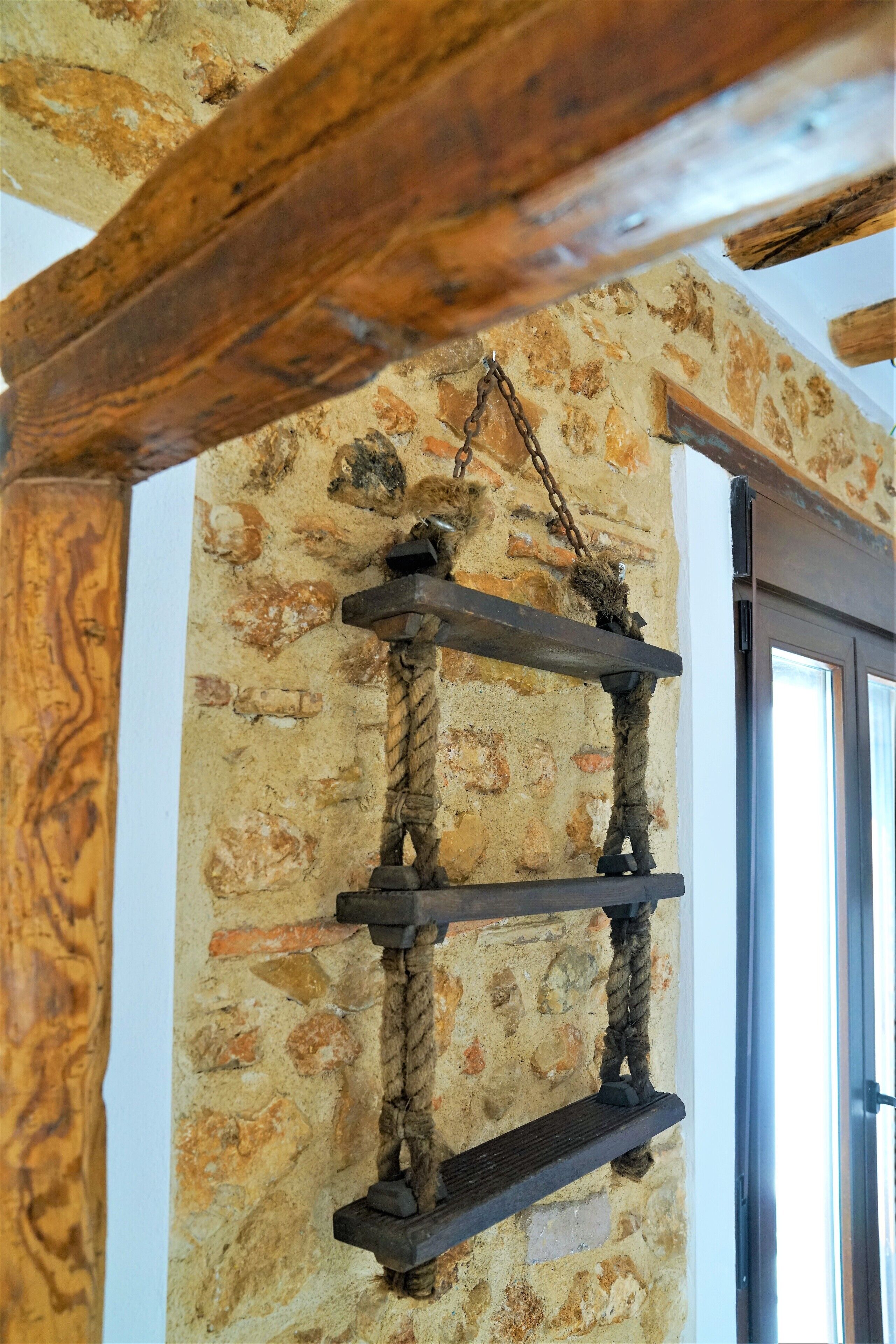Una struttura in legno rustico con elementi in corda e metallo, a contrasto con un muro in pietra.