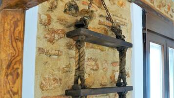 Una struttura in legno rustico con elementi in corda e metallo, a contrasto con un muro in pietra.