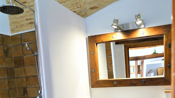 Une salle de bain avec un lavabo blanc, un meuble-lavabo en bois, un miroir et un espace douche.
