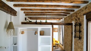 Quarto com cama, estantes brancas, luminária pendente e parede de pedra.