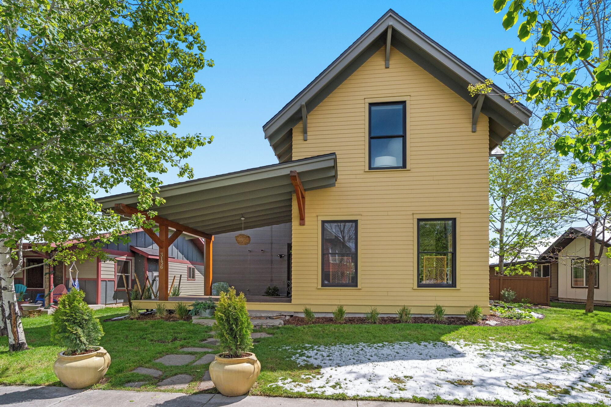 A two-story house with a gabled roof, a covered porch, and a small front yard with potted plants.