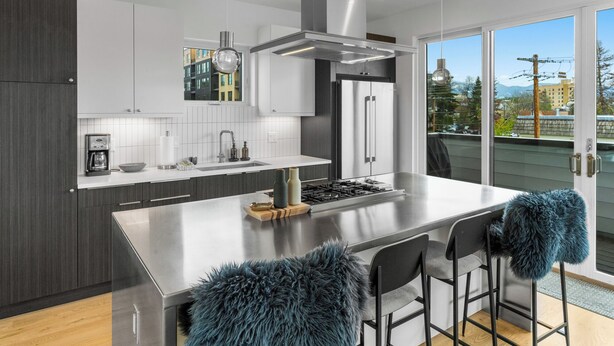 Une cuisine moderne dotée d’un îlot central, d’appareils électroménagers en acier inoxydable et offrant une vue sur la ville grâce à de grandes fenêtres.