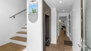 Un intérieur moderne avec un escalier, un couloir menant à une salle à manger, et une vue sur l’extérieur par une fenêtre.