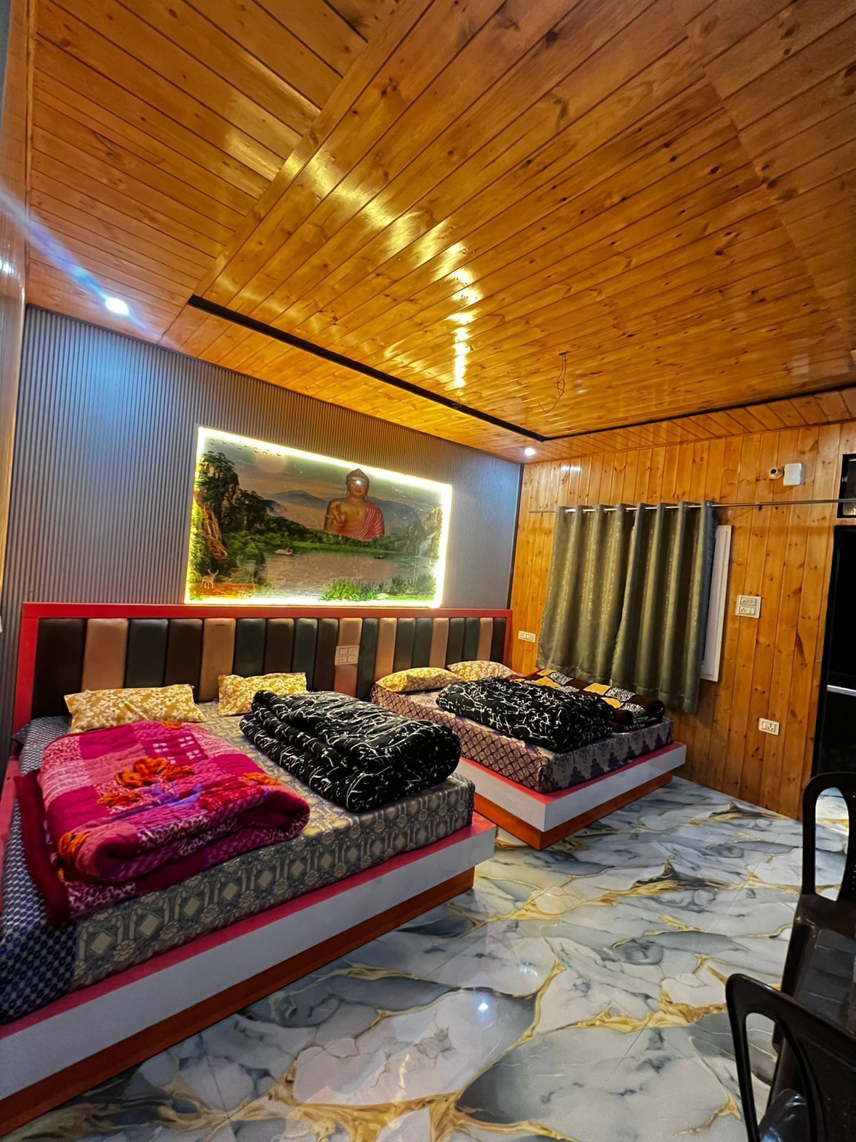 Une pièce avec un plafond en bois, un lit recouvert d’une couvre-lit à motifs, un téléviseur fixé au mur et un sol en marbre.