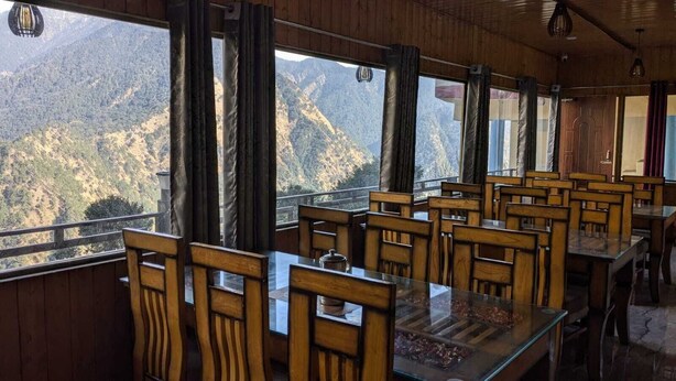 Un restaurante con mesas y sillas de madera, y amplios ventanales que ofrecen vistas a la montaña.