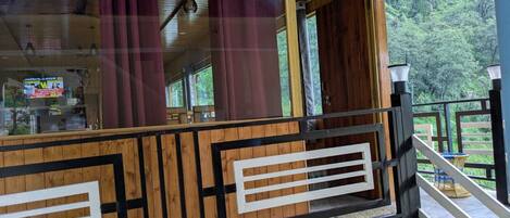 A wooden building with a balcony, a staircase, and a view of greenery.