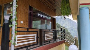 Un edificio de madera con un balcón, vistas de un paisaje montañoso y plantas colgantes.