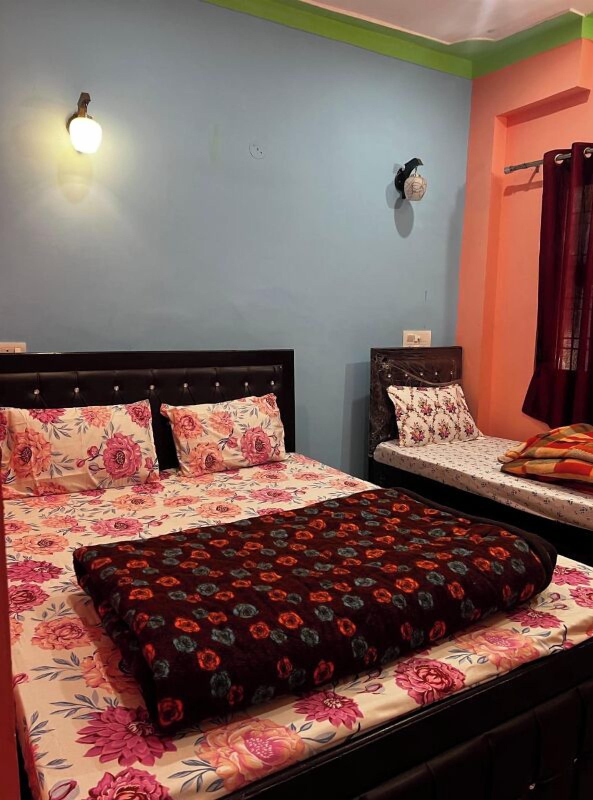 A bedroom with two beds, floral bedding, a wall-mounted light, and a decorative wall hanging.