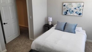 Une chambre à coucher avec un lit, des oreillers, une table de chevet, une lampe et un tableau au mur.