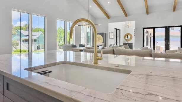 A spacious kitchen with a large island, a gold faucet, and a view of a green landscape through large windows. - 4 BR Luxury Home w Private Pool | New Renovation (Isle of Palms)