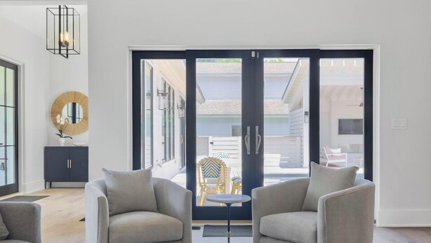 Un salon moderne avec une table basse en verre, deux fauteuils et une vue sur une terrasse extérieure, accessible par de grandes portes coulissantes.