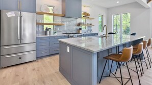 A modern kitchen with stainless steel appliances, a marble island, and bar stools. - 4 BR Luxury Home w Private Pool | New Renovation (Isle of Palms)