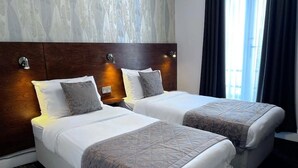 A hotel room with two beds, a wooden headboard, and a window with curtains. - Lidos Hotel (London)