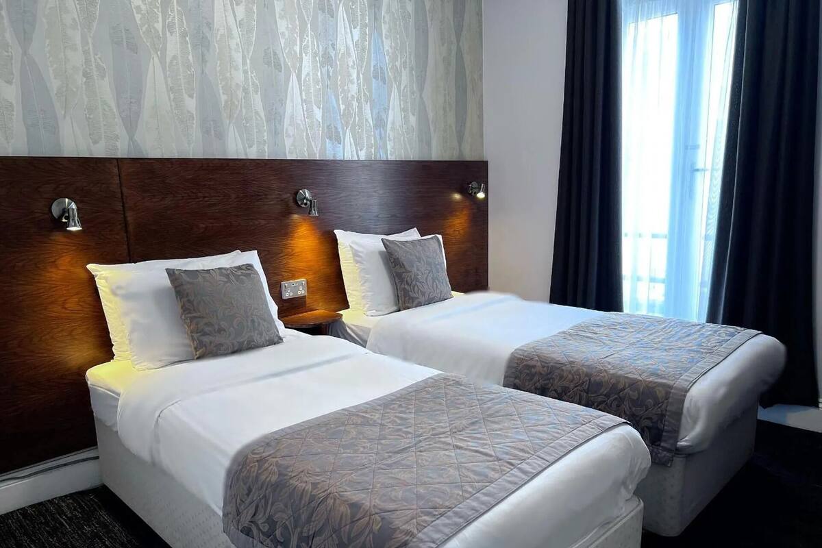 Une chambre d’hôtel avec deux lits, une tête de lit en bois et une fenêtre avec des rideaux.
