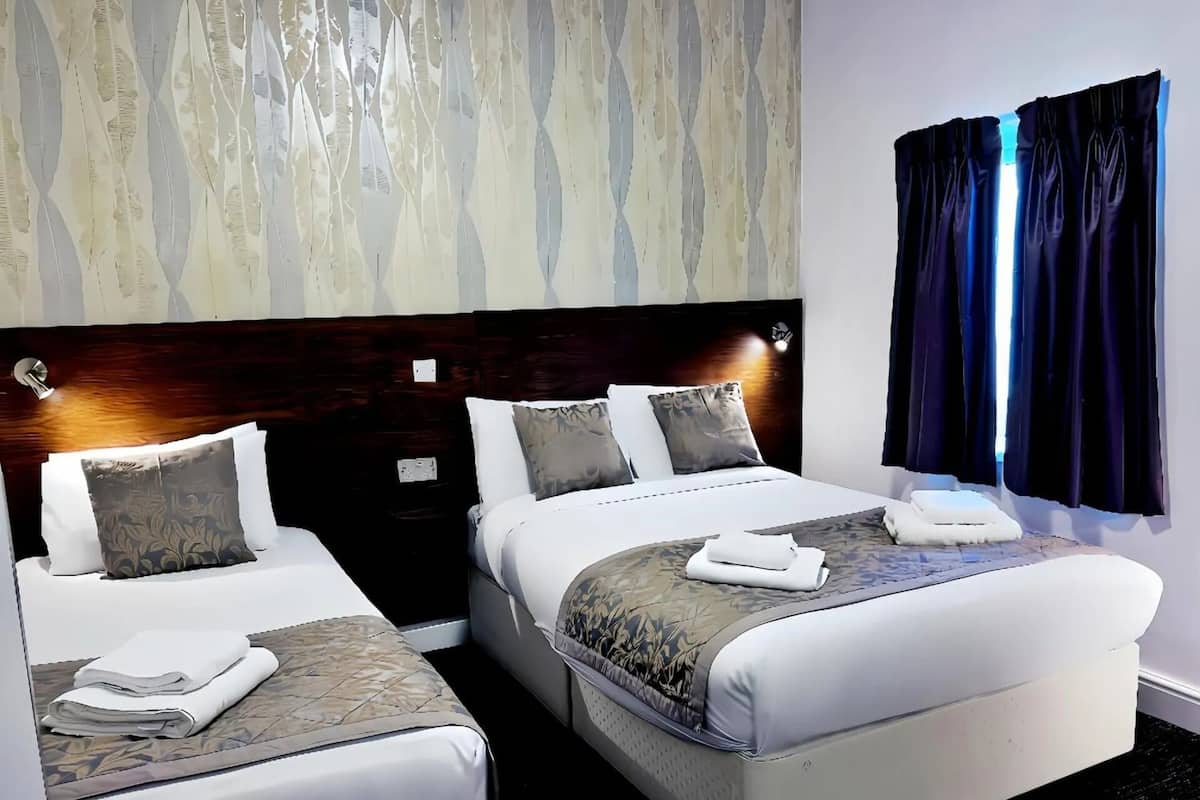 Une chambre d’hôtel avec deux lits, une tête de lit en bois foncé et une fenêtre avec des rideaux sombres.