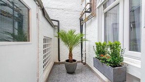 A narrow corridor with a potted palm tree, a concrete planter with green shrubs, and a window with a white frame. - Lidos Hotel (London)