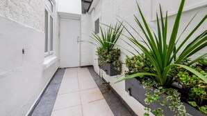 A narrow corridor with white walls, tiled flooring, and potted plants on the right. - Lidos Hotel (London)