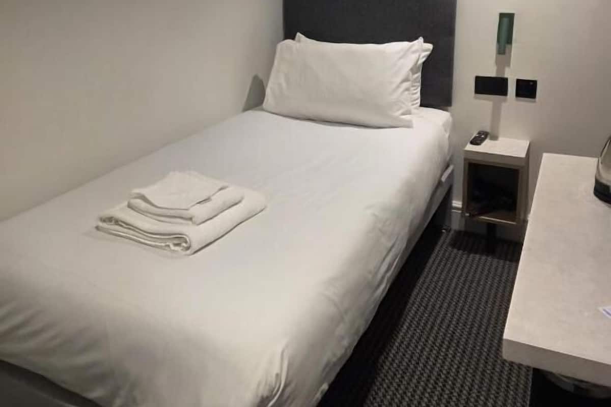 Une chambre d’hôtel avec un lit bien fait, une table de chevet avec une lampe et une petite commode.