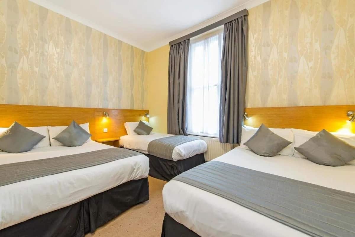 Une chambre d’hôtel avec deux lits, chacun doté d’une tête de lit, d’une literie grise et d’une fenêtre avec des rideaux.