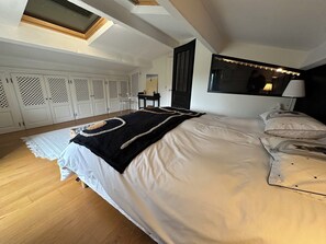 Relax in this serene bedroom with a large bed, wooden floor, and a skylight above.
