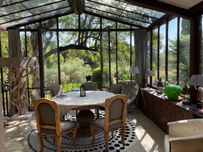 Enjoy meals in this serene conservatory-style room with a round dining table and four chairs, overlooking a lush garden.