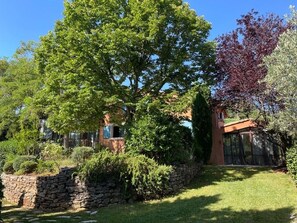 Stroll through the beautifully maintained garden, surrounded by a variety of trees and shrubs, and a charming house with large windows.