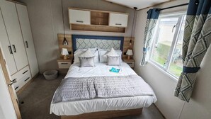 Un dormitorio con cama, mesitas de noche, armario y ventana con cortinas.