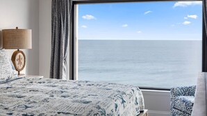 Een slaapkamer met een groot raam met uitzicht op zee.