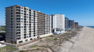 Un hotel frente a la playa con varios pisos, balcones y un acceso directo a la playa.