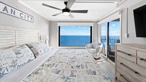 Een slaapkamer met een groot bed, een plafondventilator, uitzicht op de oceaan en een bord met de tekst 
